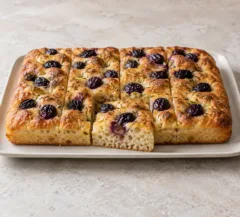 Focaccia dorée aux raisins noirs et au romarin, mie visible sur une part