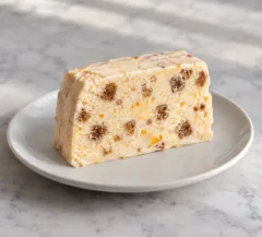 Tranche de parfait glacé à l’orange avec petits morceaux de pain d’épices dans une base ivoire